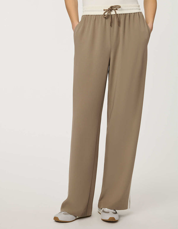 Woman wearing a pull-on wide leg trouser with side stripe in taupe, featuring elastic drawstring waistband and relaxed fit.